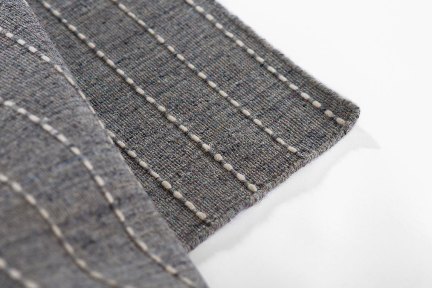 Gray-blue woven rug with white topstitching in parallel lines along the edge.