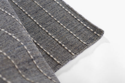 Gray-blue woven rug with white topstitching in parallel lines along the edge.