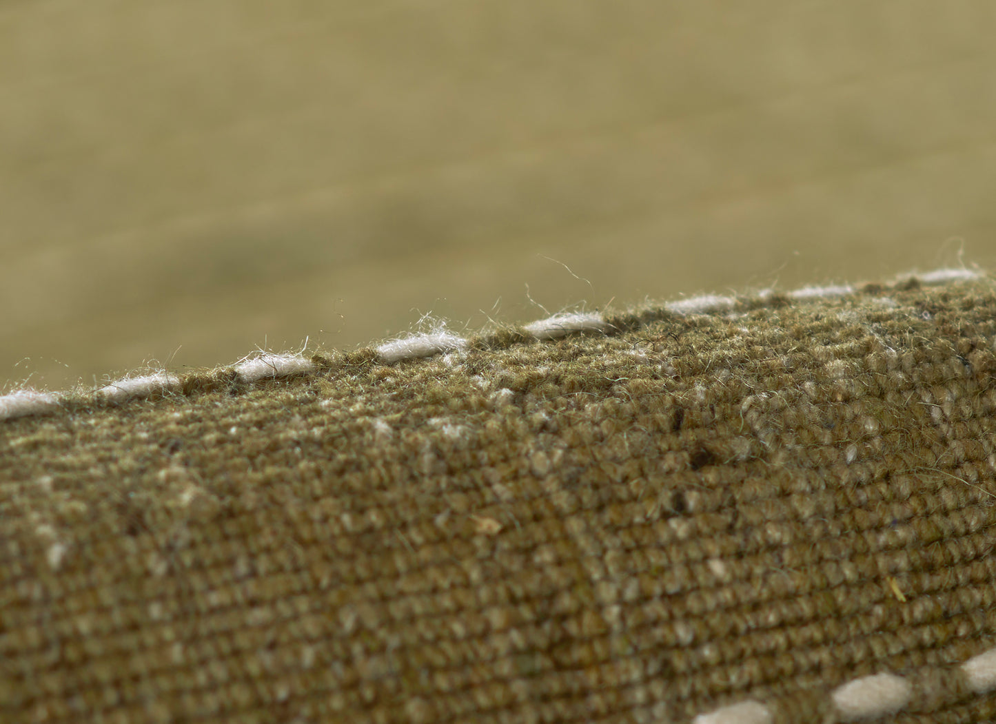 Olive green coarse woven rug close-up with white fringe along the edge.