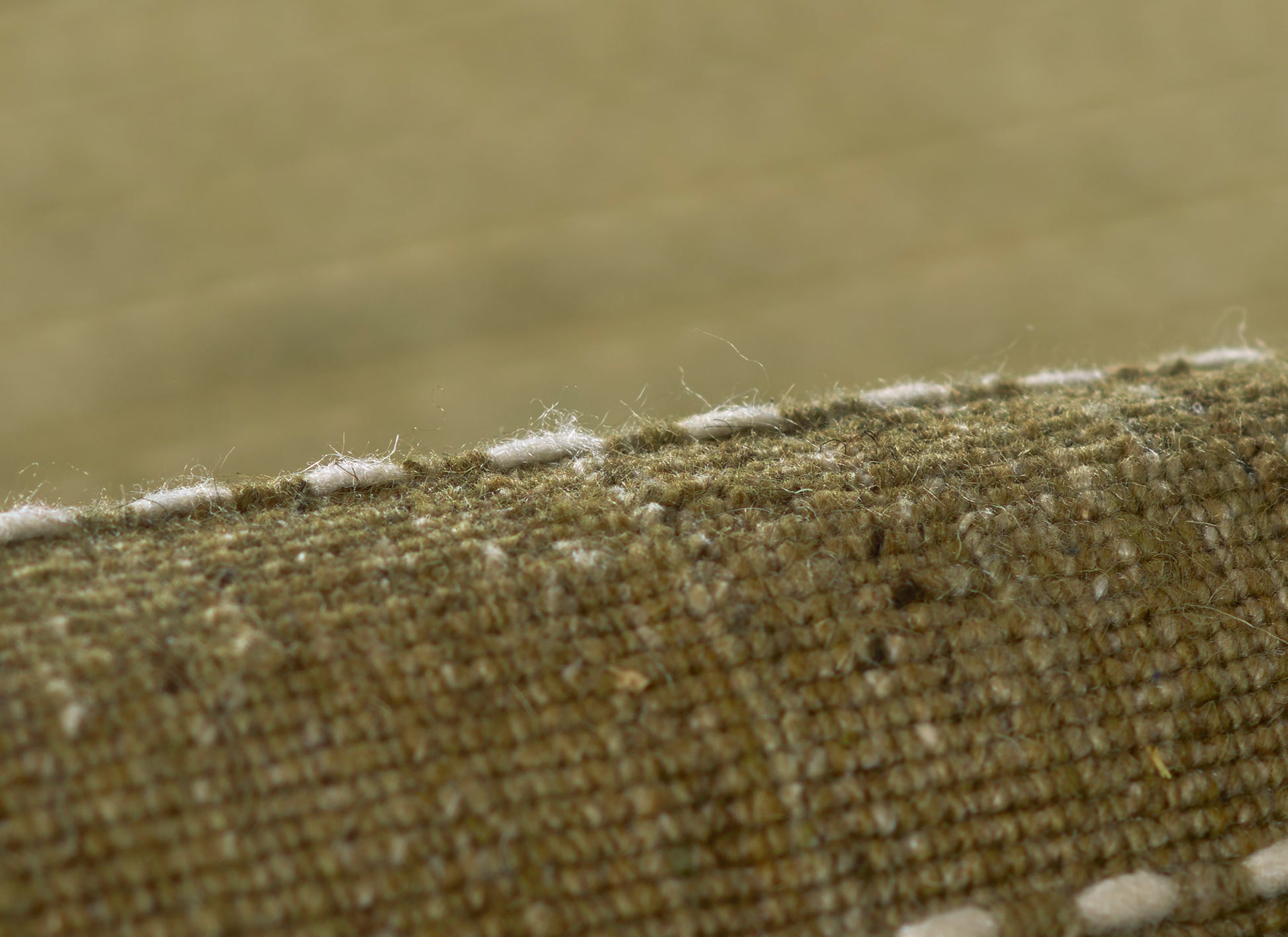 Olive green coarse woven rug close-up with white fringe along the edge.