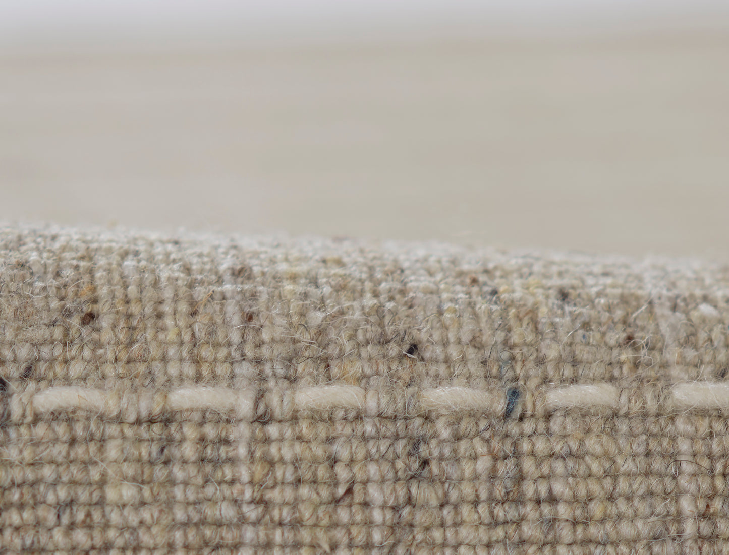 Natural beige woven rug close-up; textured jute fibers and stitched edge.