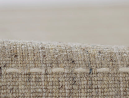 Natural beige woven rug close-up; textured jute fibers and stitched edge.