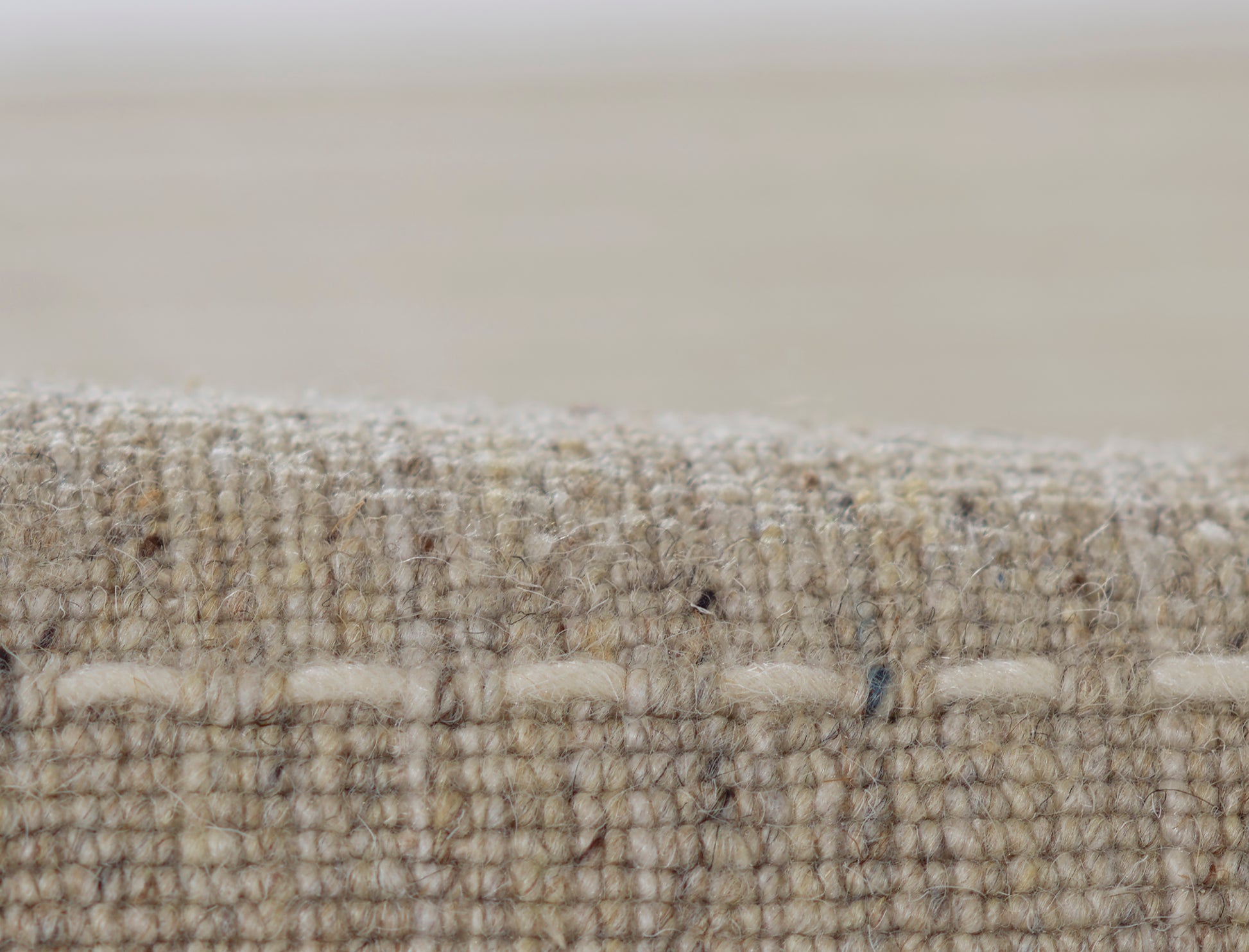 Close-up of a natural-fiber woven rug edge with thick loops and textured fibers; rustic neutral decor.