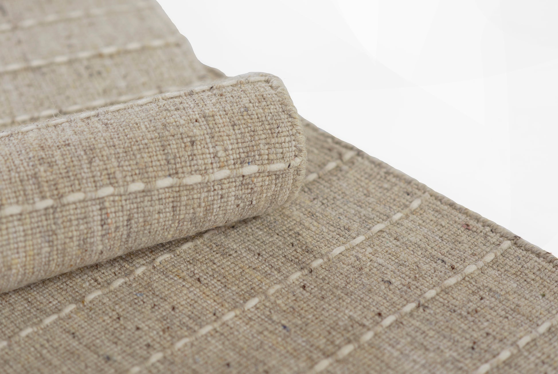 Natural beige jute rug with woven flatweave texture, white stitched edges, rolled corner detail.