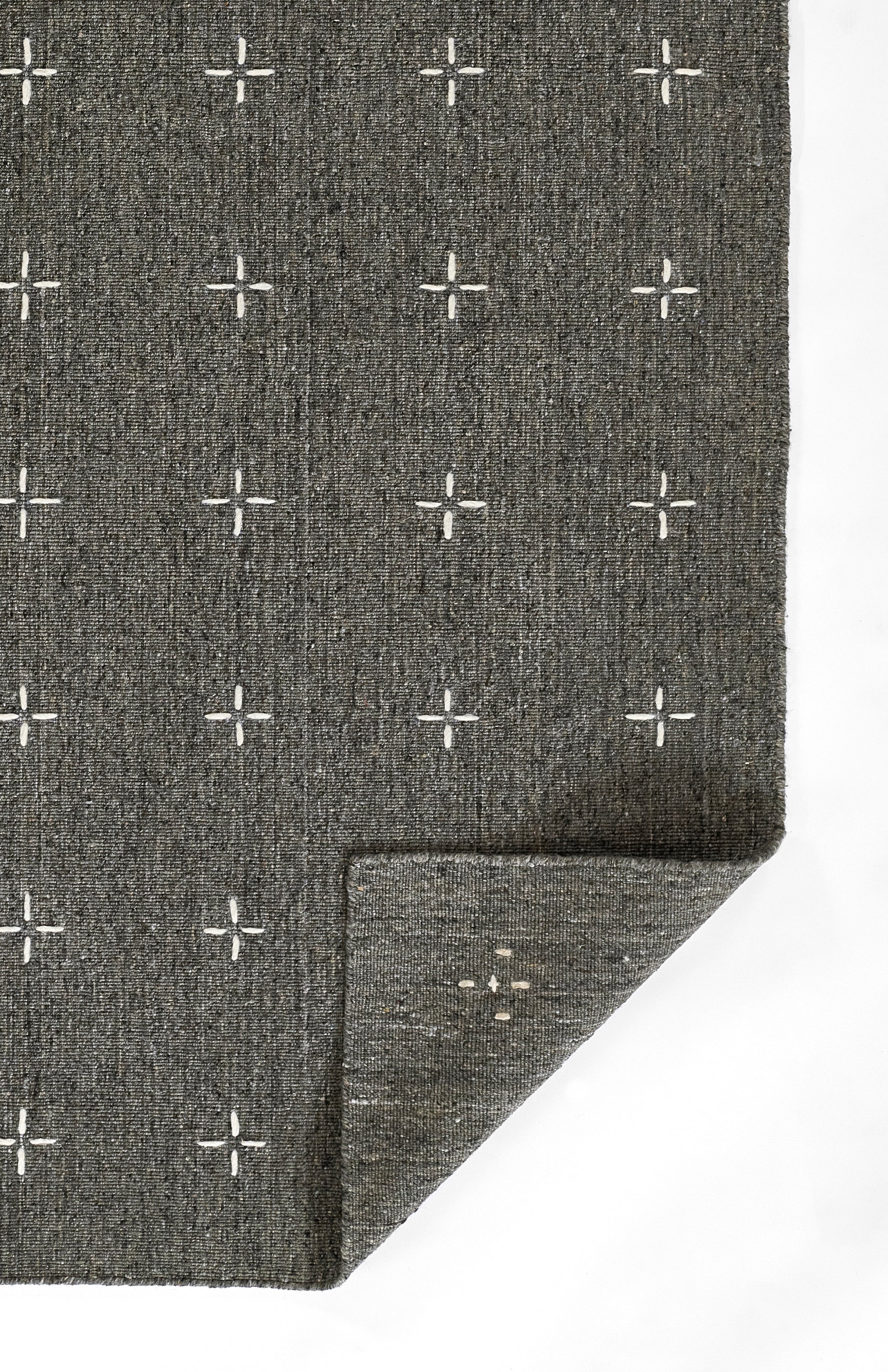 Charcoal gray woven rug with white plus-sign grid pattern; textured fabric with folded corner.