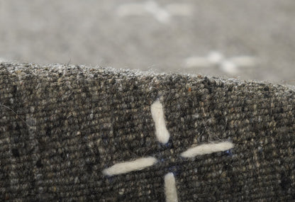 Close-up of olive-gray tweed fabric with white cross-stitch motif; textured wool blend.