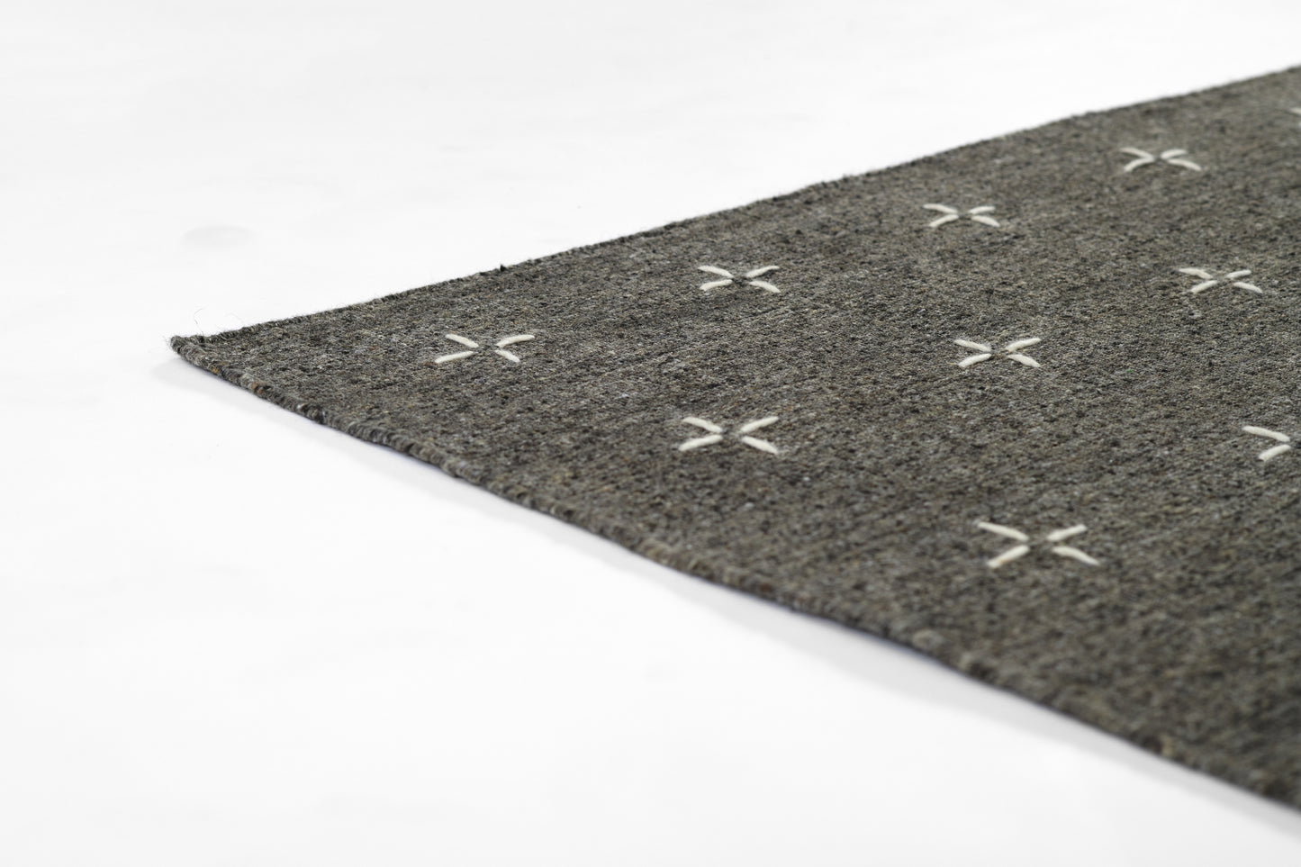 Gray textured rug with white cross-stitch X pattern, close-up corner view.
