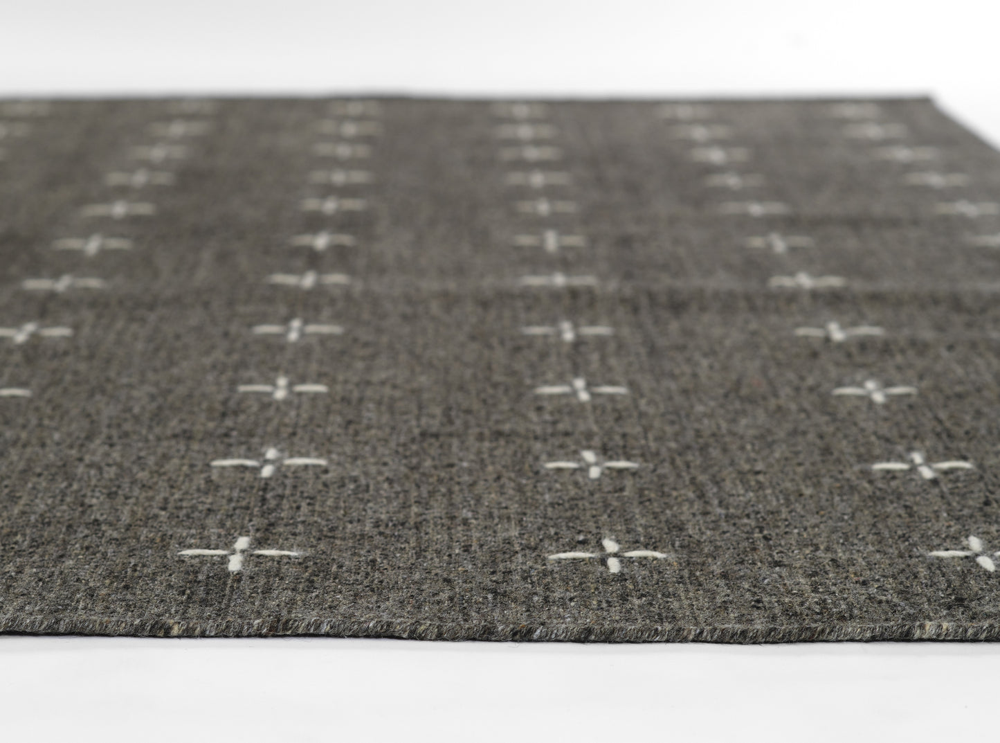 Dark gray woven rug with white cross motifs in a grid pattern.
