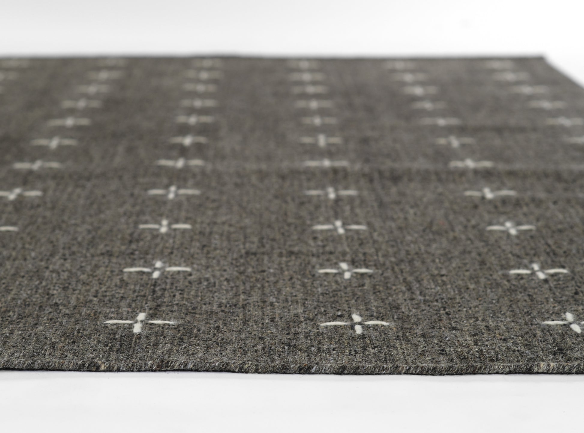 Dark gray woven rug with white cross motifs in a grid pattern.