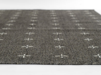 Dark gray woven rug with white cross motifs in a grid pattern.