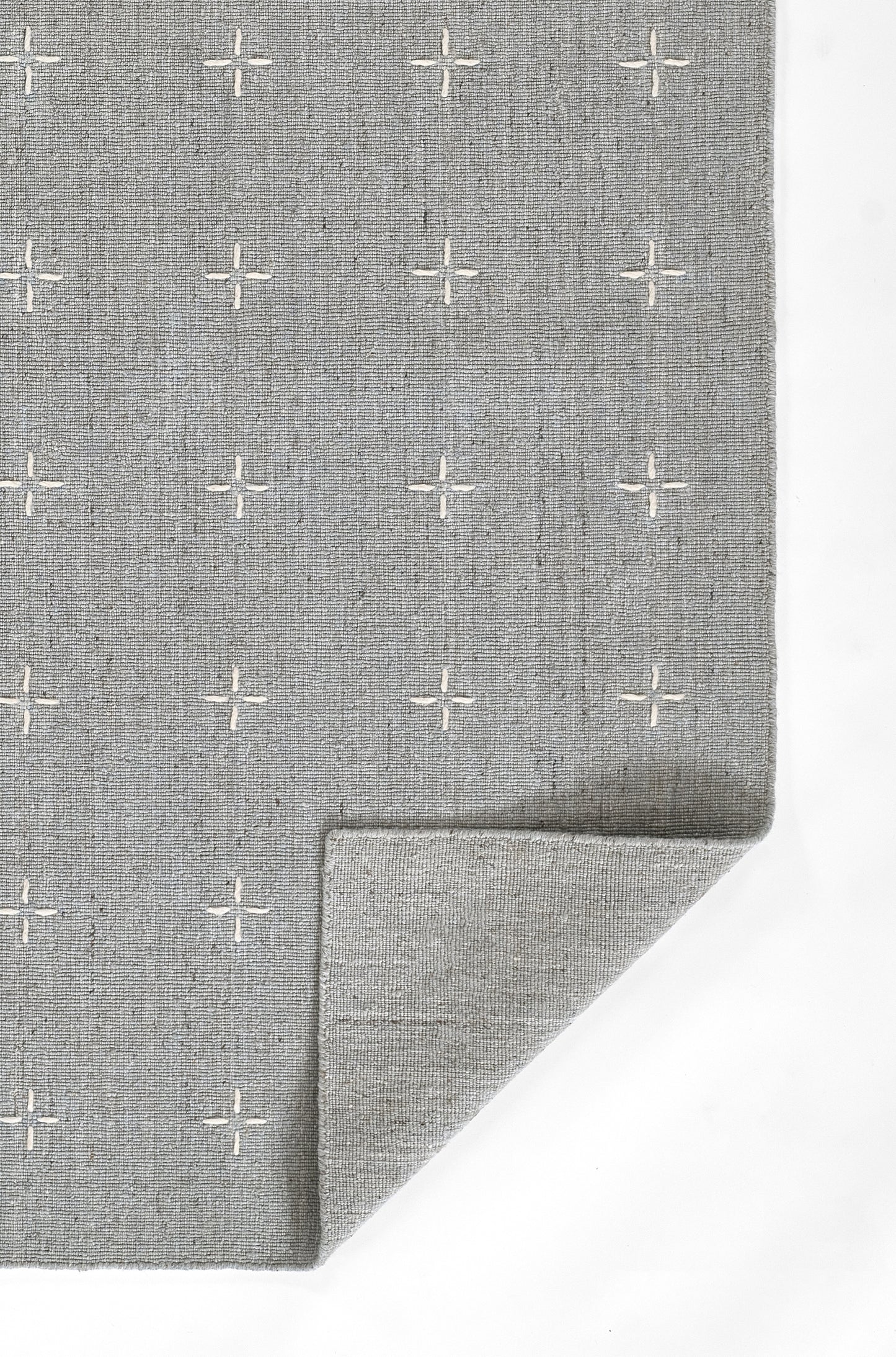 Gray woven rug with white plus-sign pattern, soft textured fabric, folded corner.