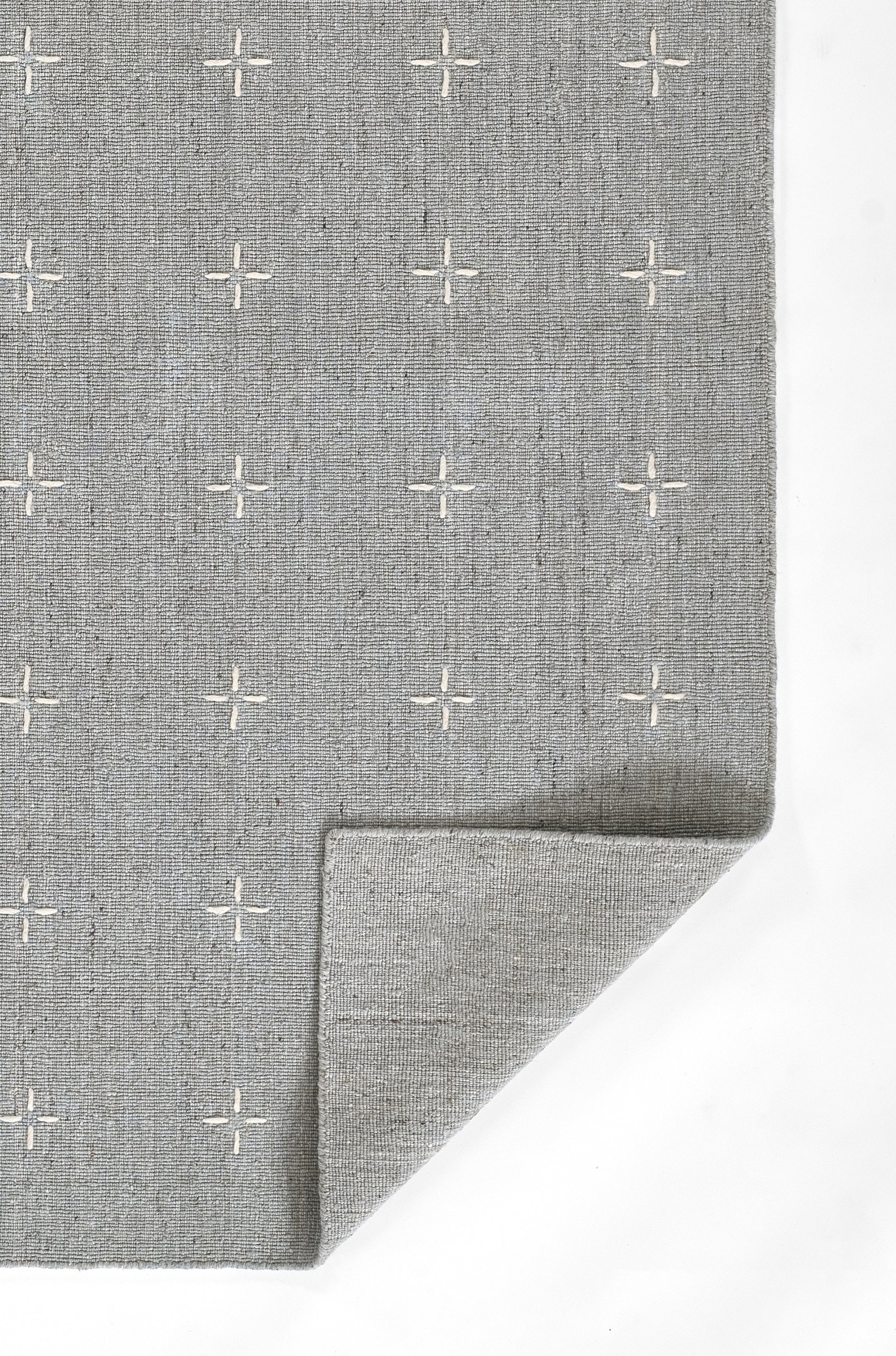 Gray woven rug with white plus-sign pattern, soft textured fabric, folded corner.