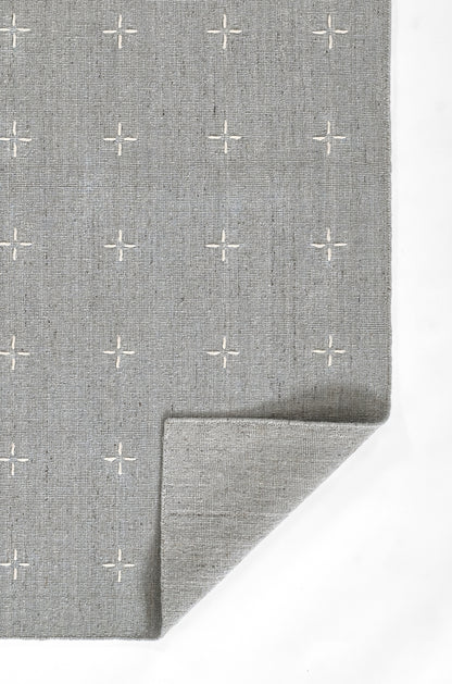 Gray woven rug with small white plus sign motifs, textured surface, folded corner