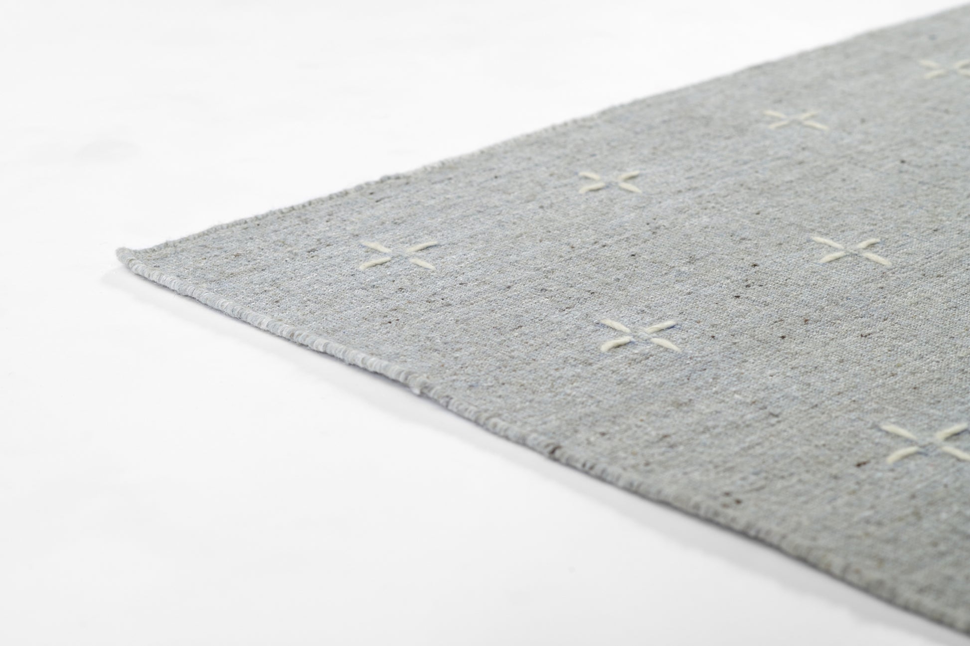 Gray textured rug with cream X-shaped stitches and a fringed edge.