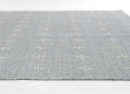 Gray-blue flatwoven rug with cream cross shapes and fringed edges.