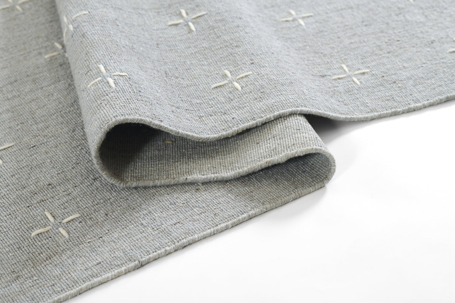 Gray woven rug with cream stitched plus signs, soft textured fabric, rolled edge.
