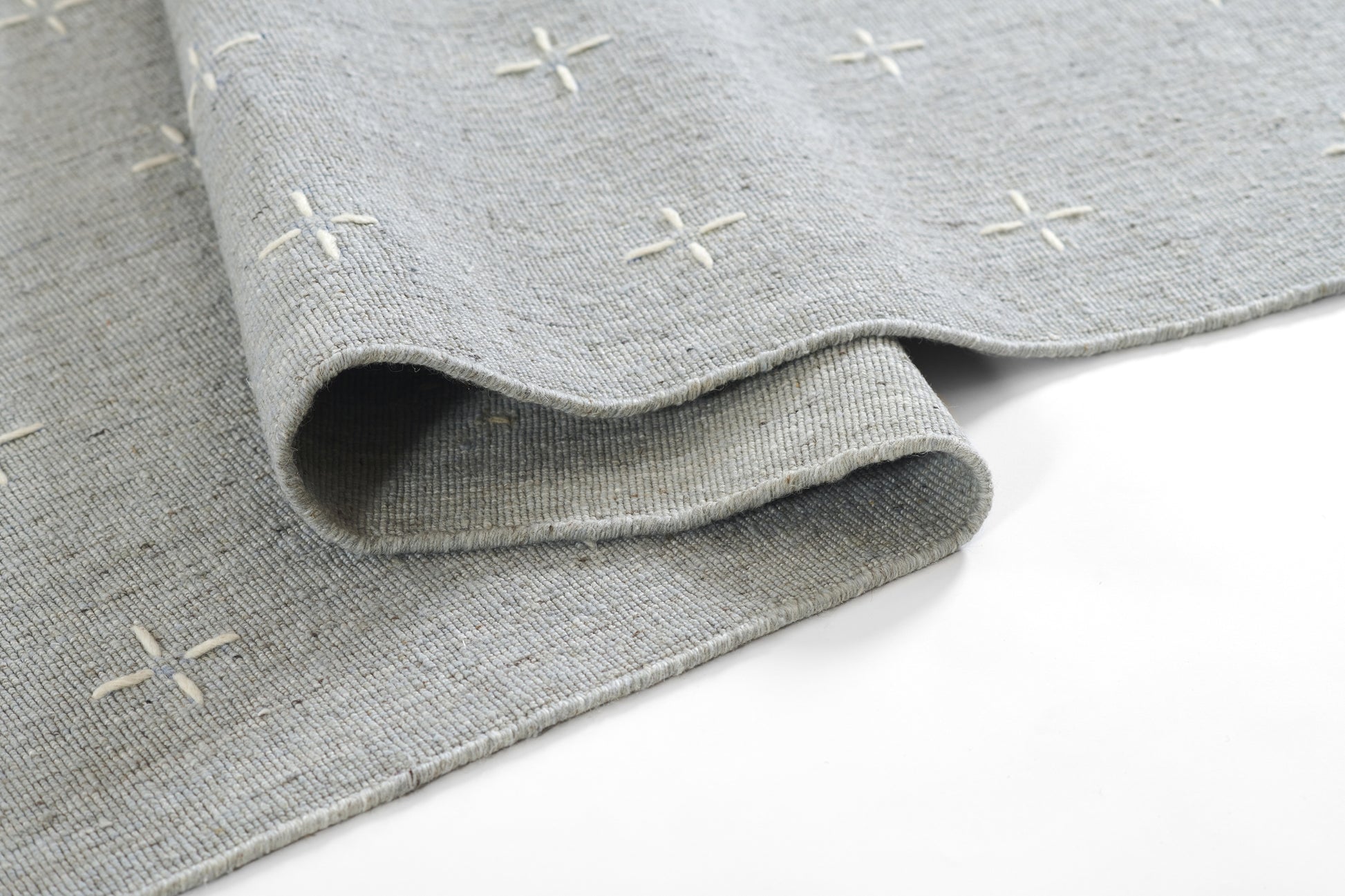 Gray woven rug with cream stitched plus signs, soft textured fabric, rolled edge.