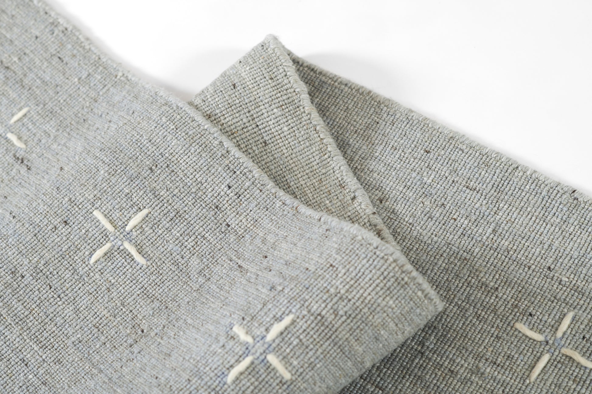 Gray rug with white X-stitch embroidery, folded to show a textured rustic surface (4' x 6').