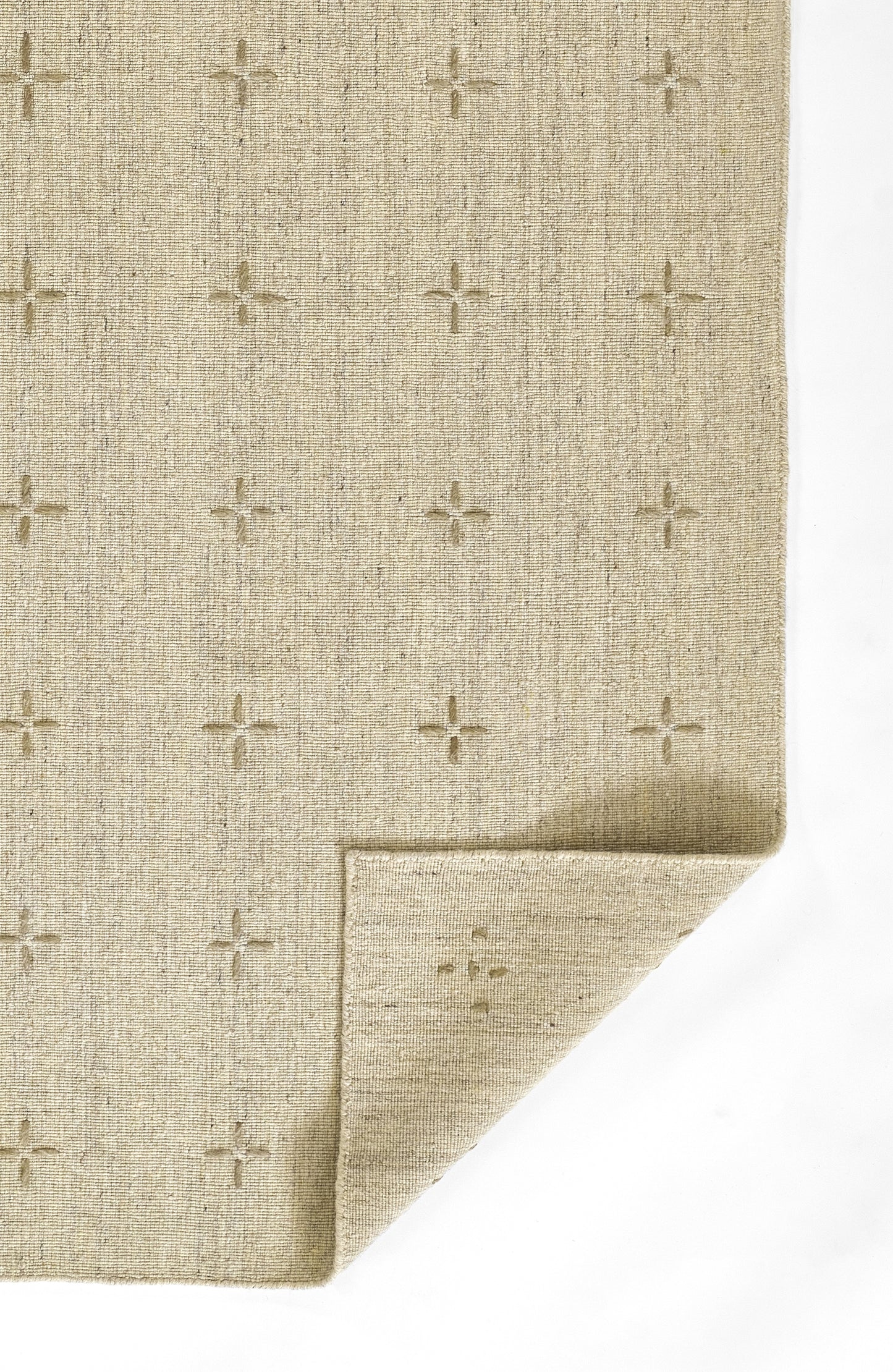 Olive-toned woven rug with subtle cross motifs in a grid; textured fibers and folded corner show thickness.