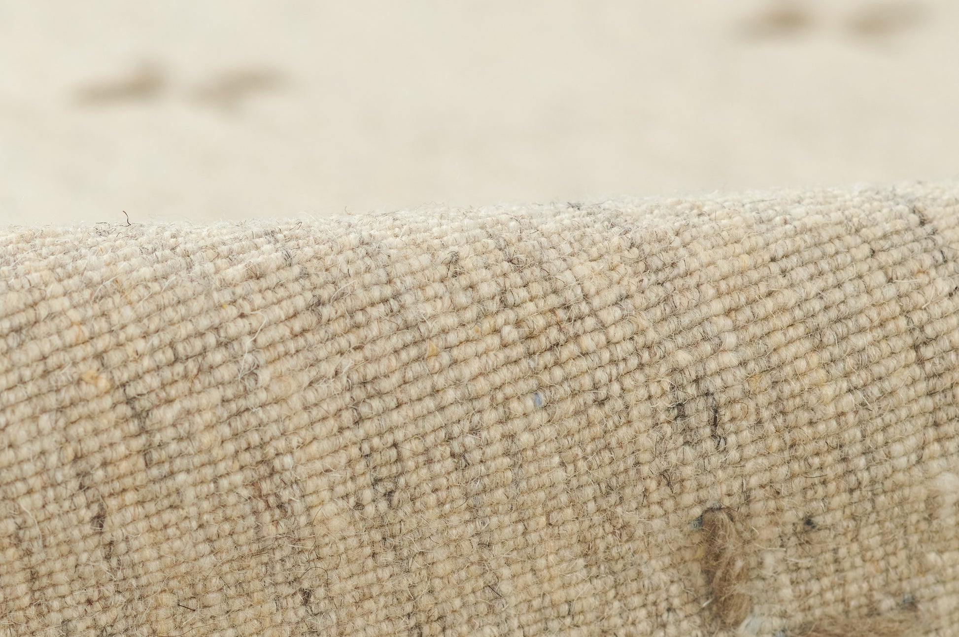 Close-up of beige natural woven rug fabric with speckled fibers and a rolled edge.