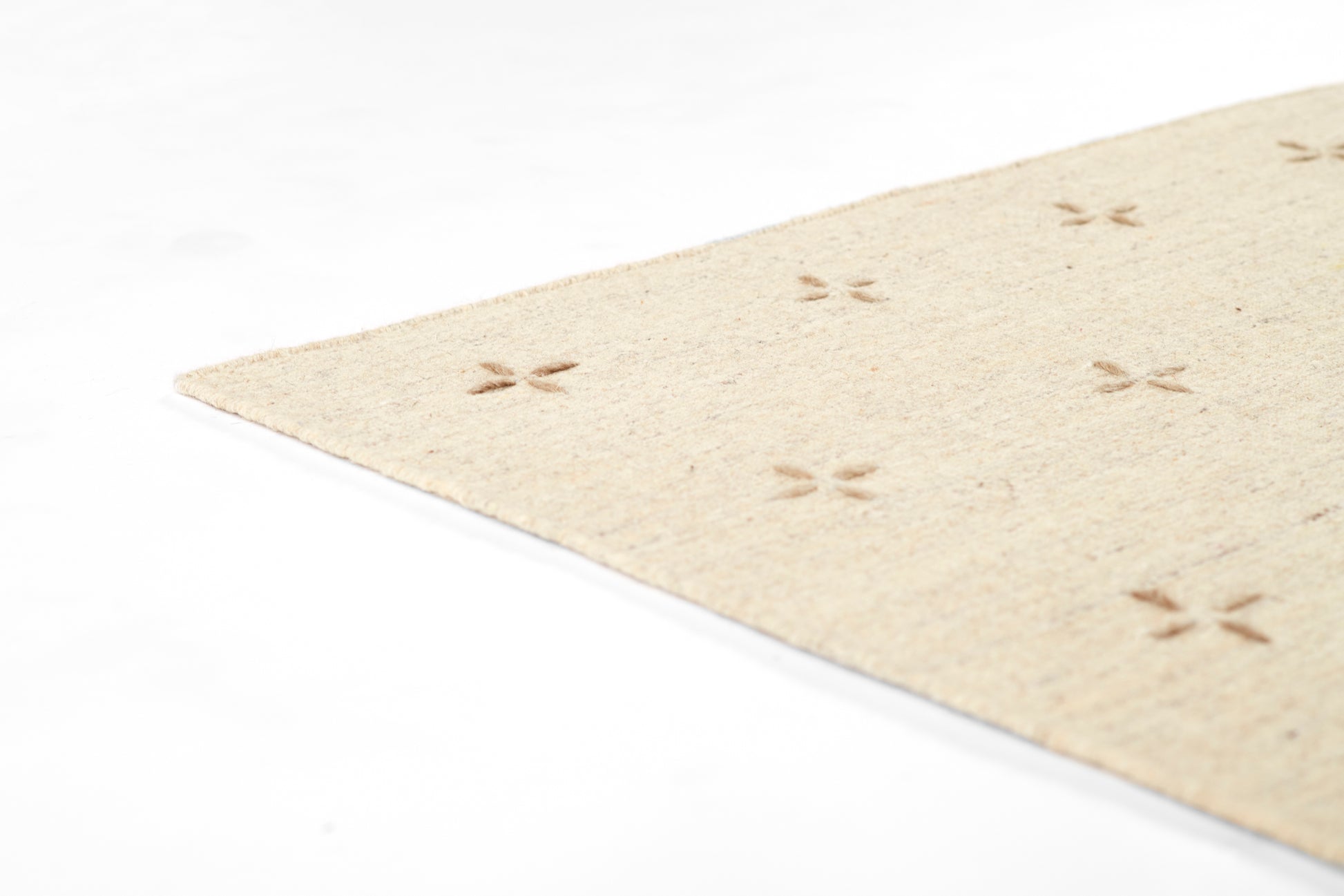 Beige natural fiber rug with small cross-shaped flower motifs in a subtle grid, shown at a diagonal corner.