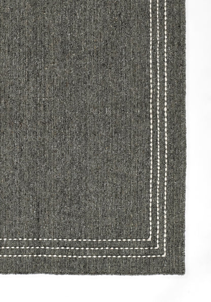 Charcoal grey textured rug with double white dashed-stitch border along the edge.
