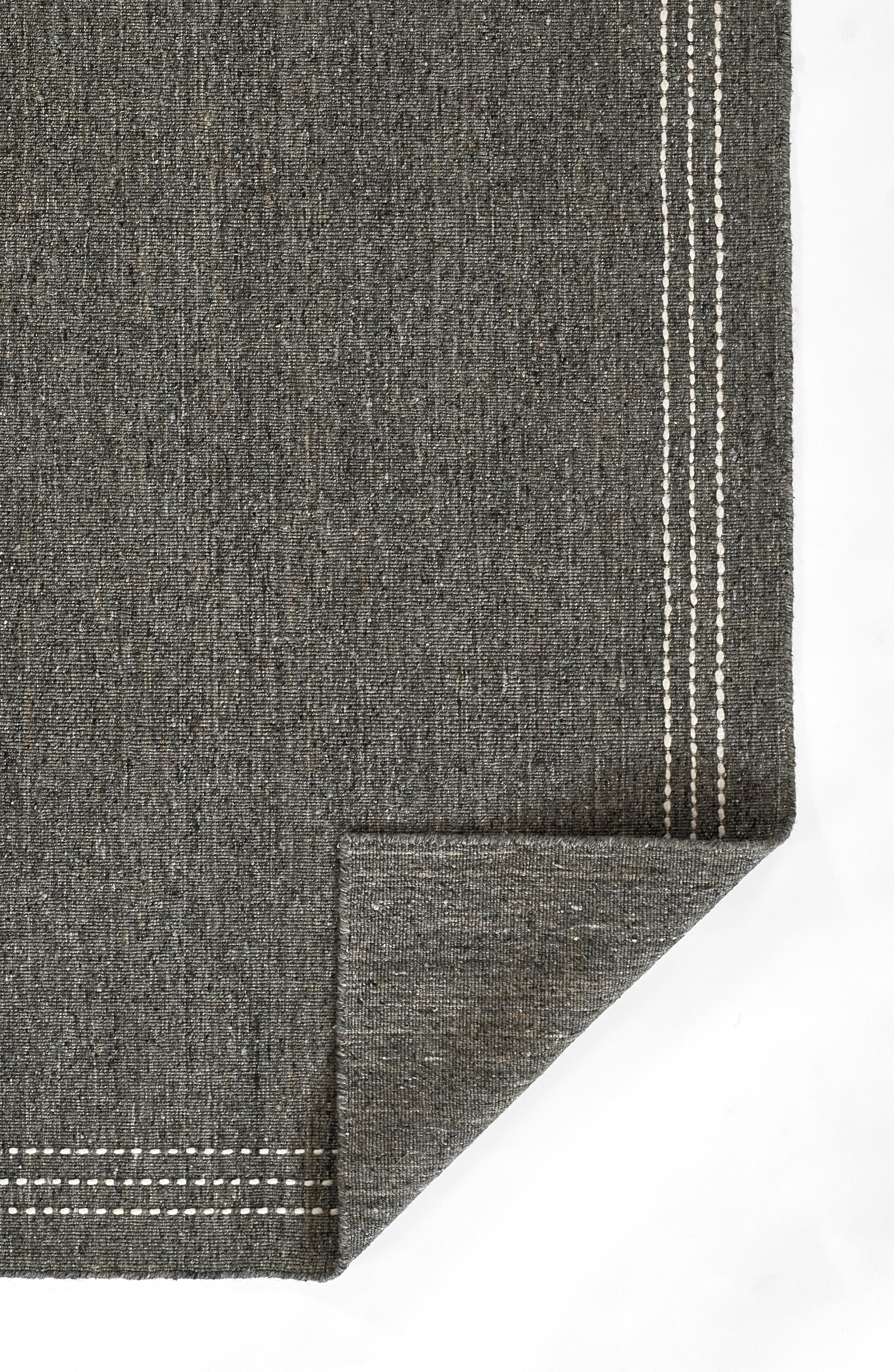 Charcoal gray woven rug with white stitched border along the edges and a folded corner.