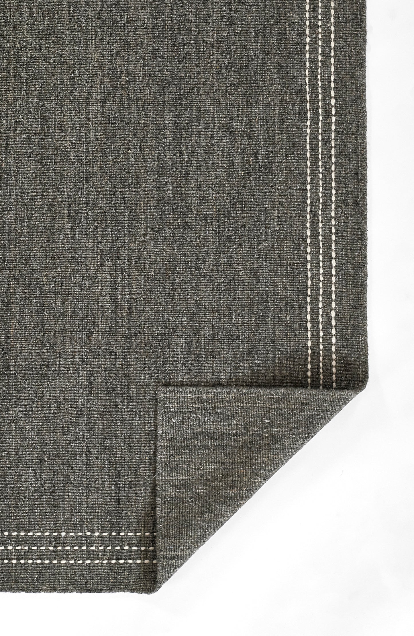 Charcoal gray woven rug with white stitched border lines; folded corner reveals underside.