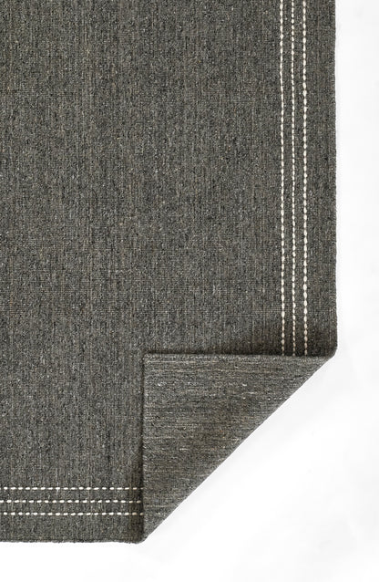 Charcoal grey woven rug with triple white stitched border, folded corner for a modern look.