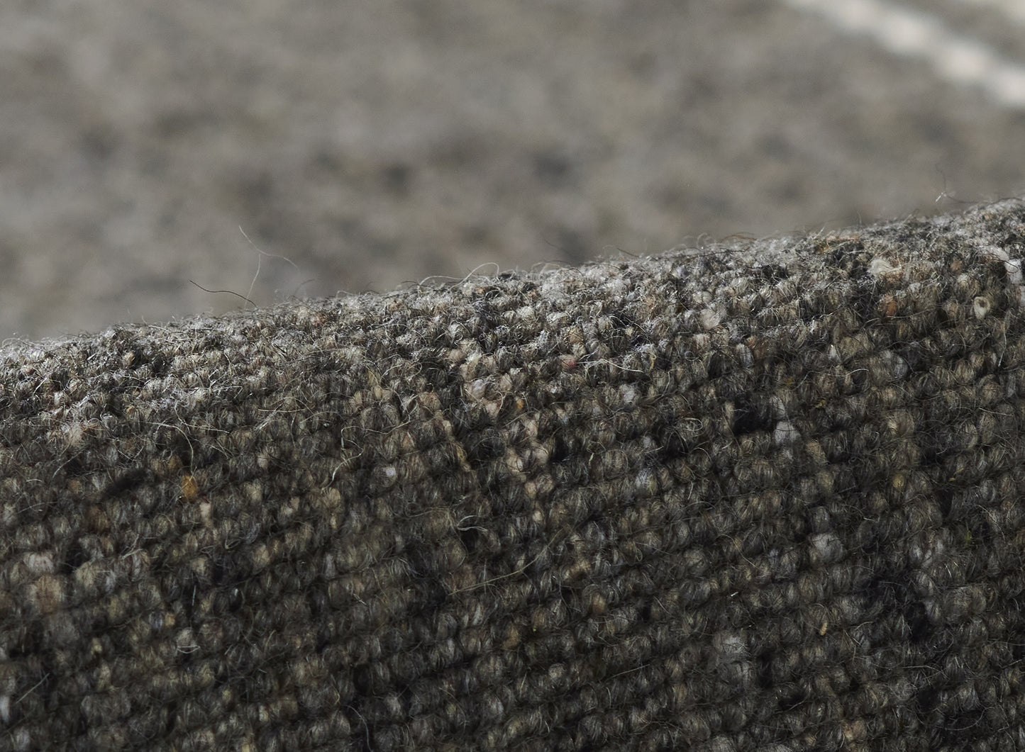 Close-up of a dark olive tweed wool rug with textured loop weave and rolled edge.