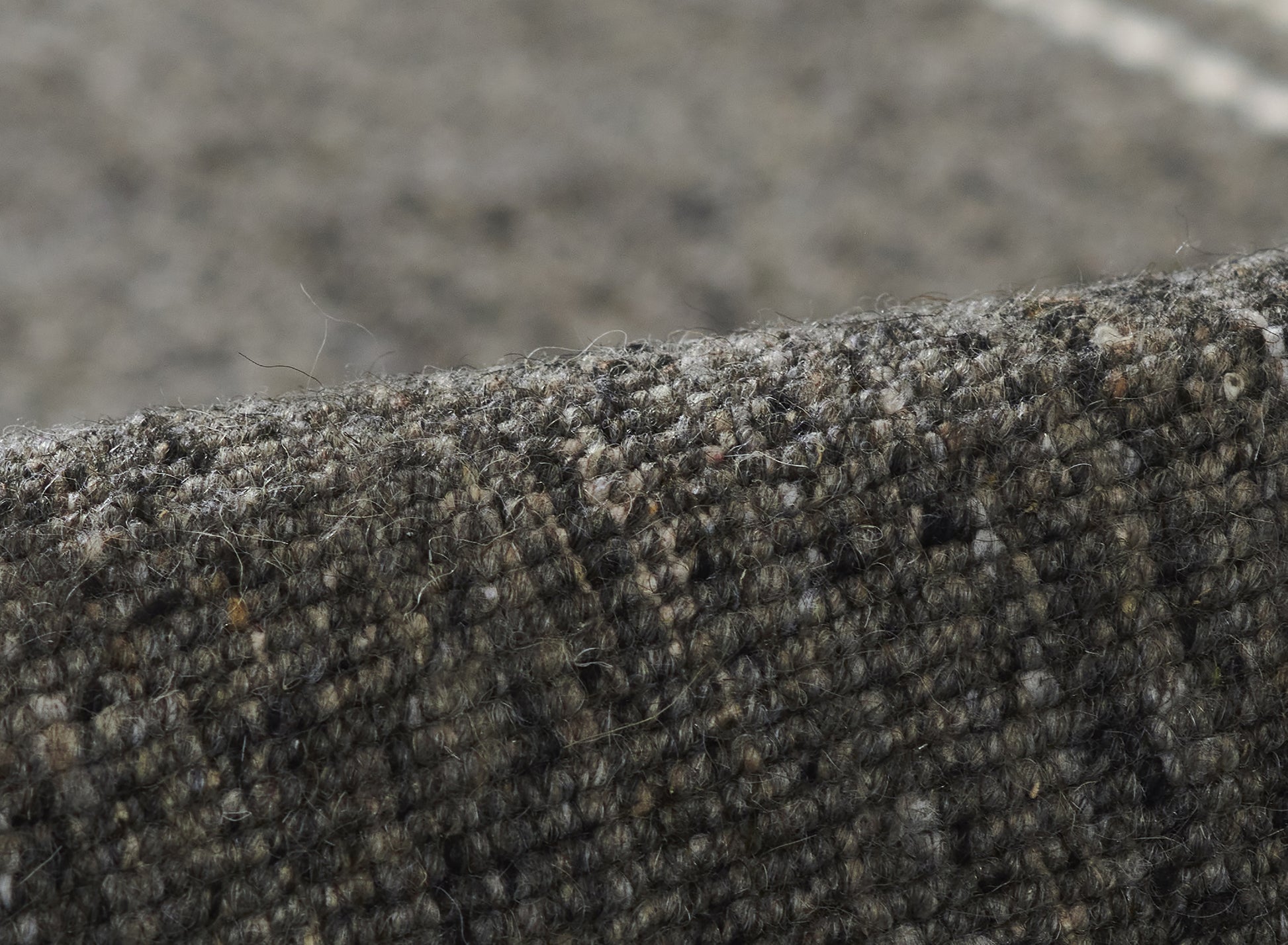 Close-up of dark olive-gray boucle tweed fabric with a textured wool blend upholstery weave.