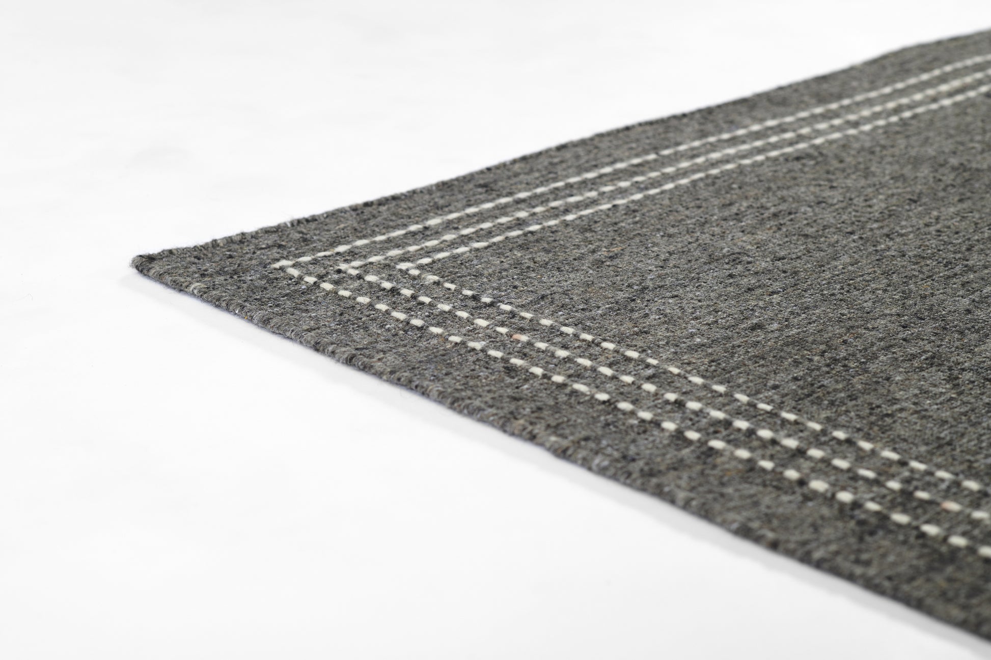 Grey textured rug edge with a white stitched border, modern minimalist floor mat.