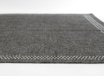 Dark grey textured flatweave rug with white stitched border, modern minimalist decor.