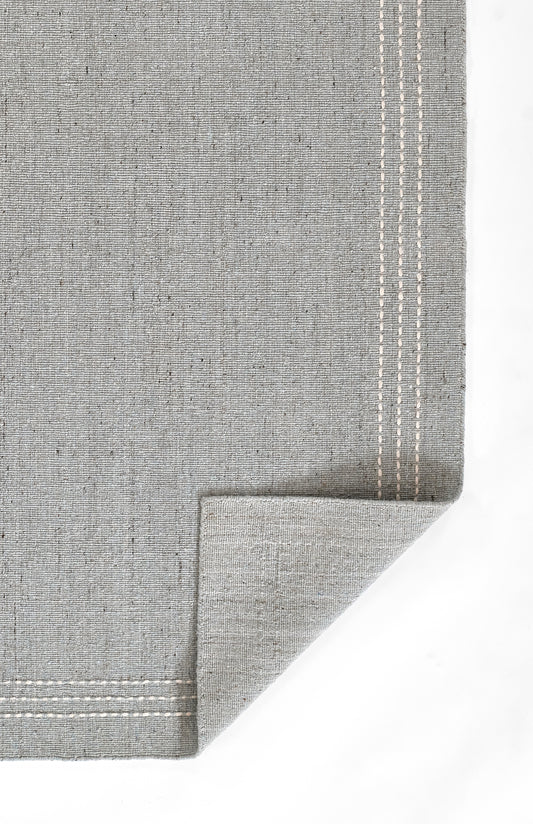 Grey linen napkin with white double-stitch border, folded corner for a casual elegant table setting.