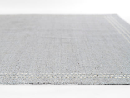Light gray woven rug with cream stitched border along the edge; minimalist, modern floor decor.