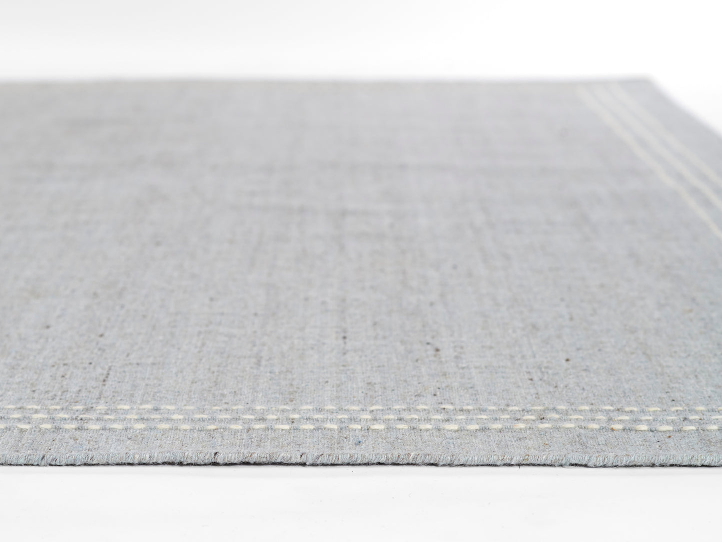 Light gray woven rug with cream stitched border & subtle texture.