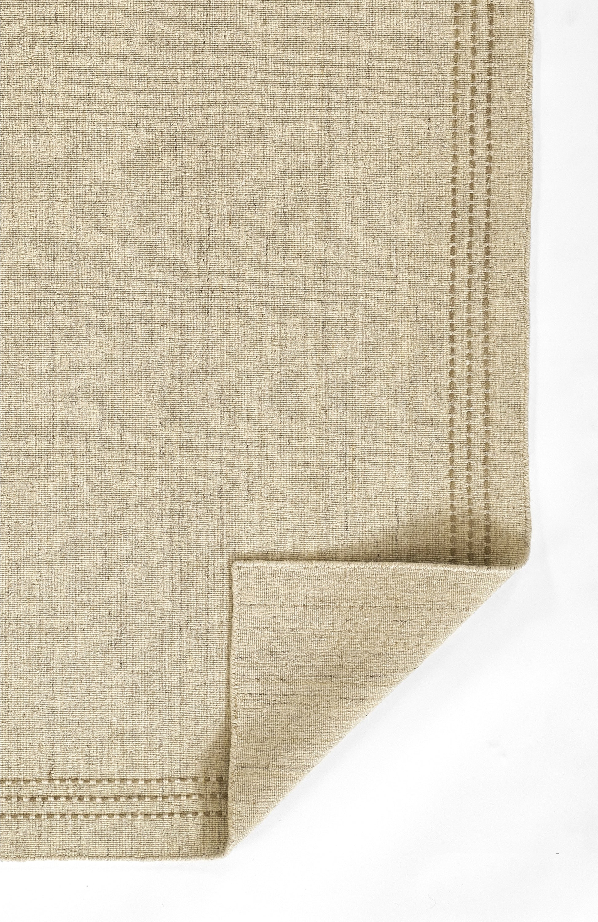 Natural beige flat-weave rug with subtle texture and stitched border along edges; folded corner.