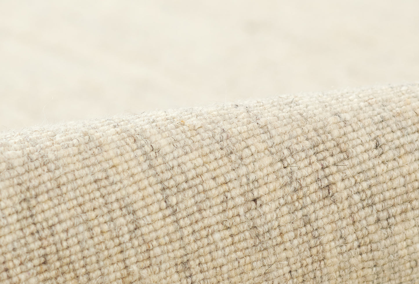 Beige woven rug close-up with rolled edge; natural fiber, chunky texture, subtle striped pattern.