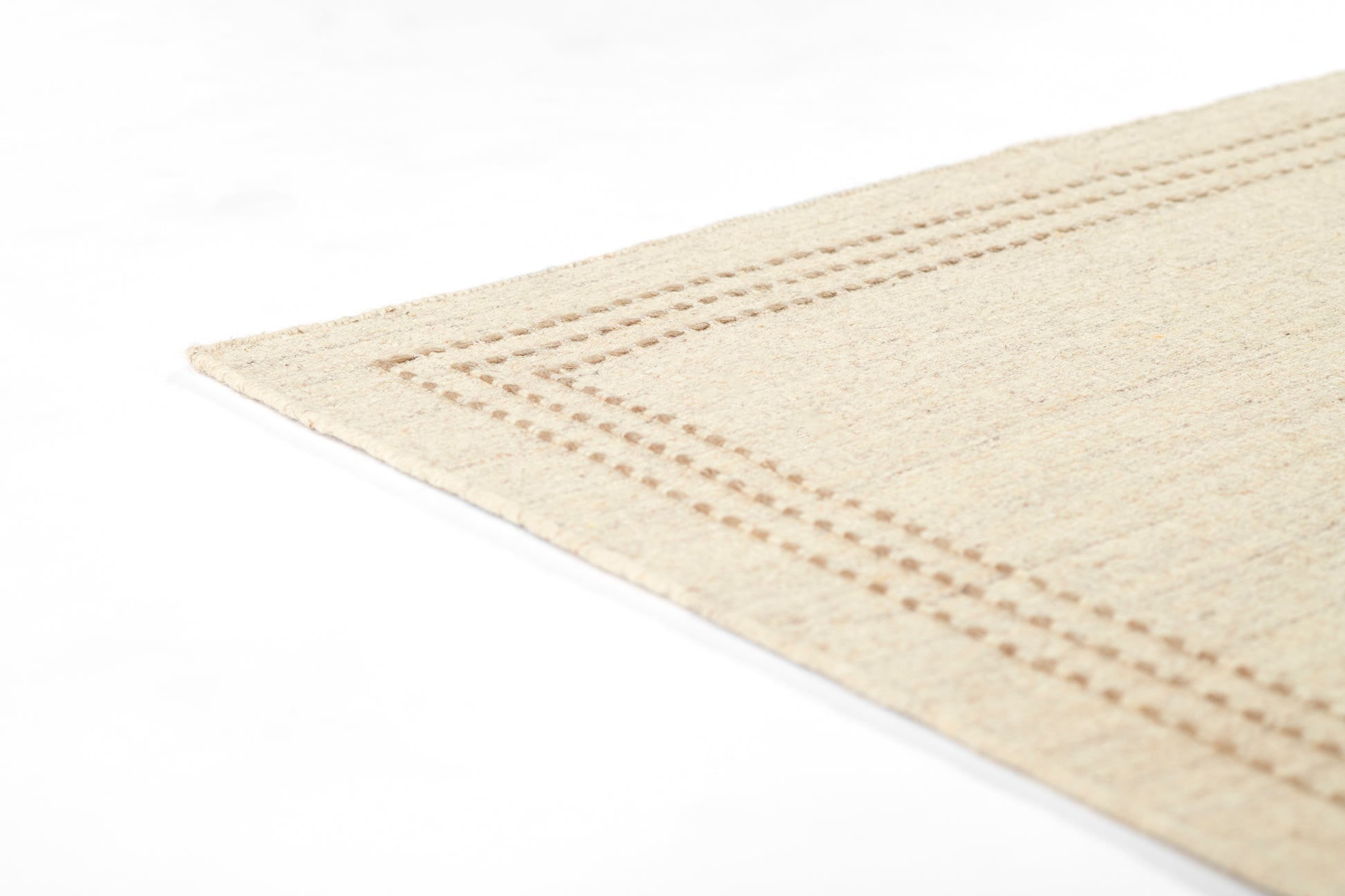 Beige natural-fiber rug with dotted stitched border along edge, corner view.