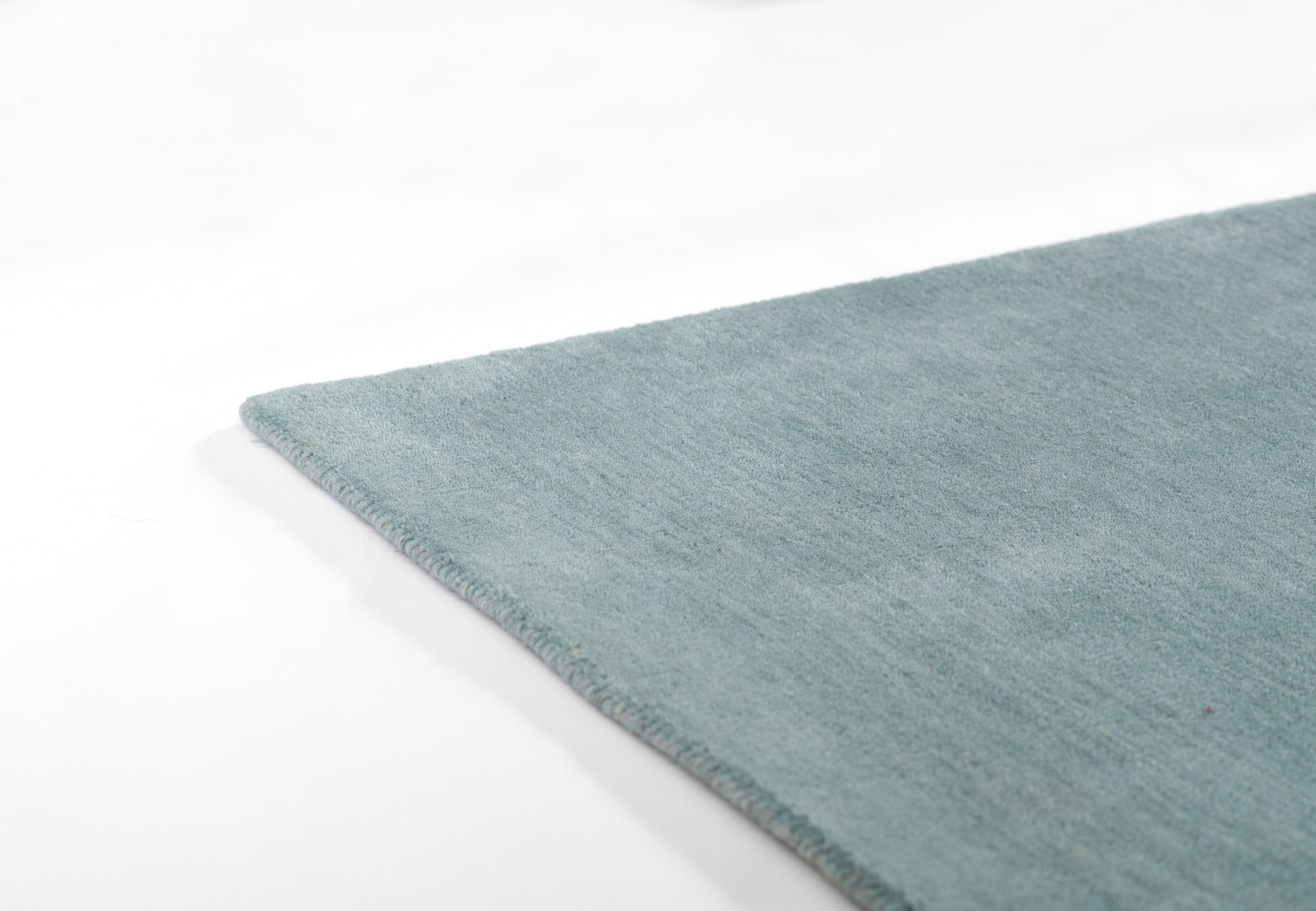 Teal blue ombre rug with soft plush pile and finished edge, angled view.
