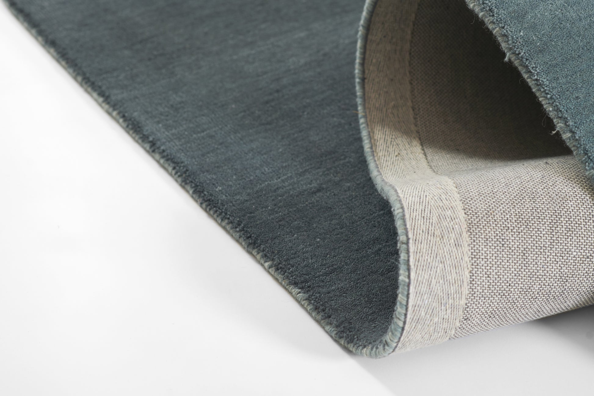 Blue ombre rug rolled up, teal-blue top with beige woven underside, soft textured pile.
