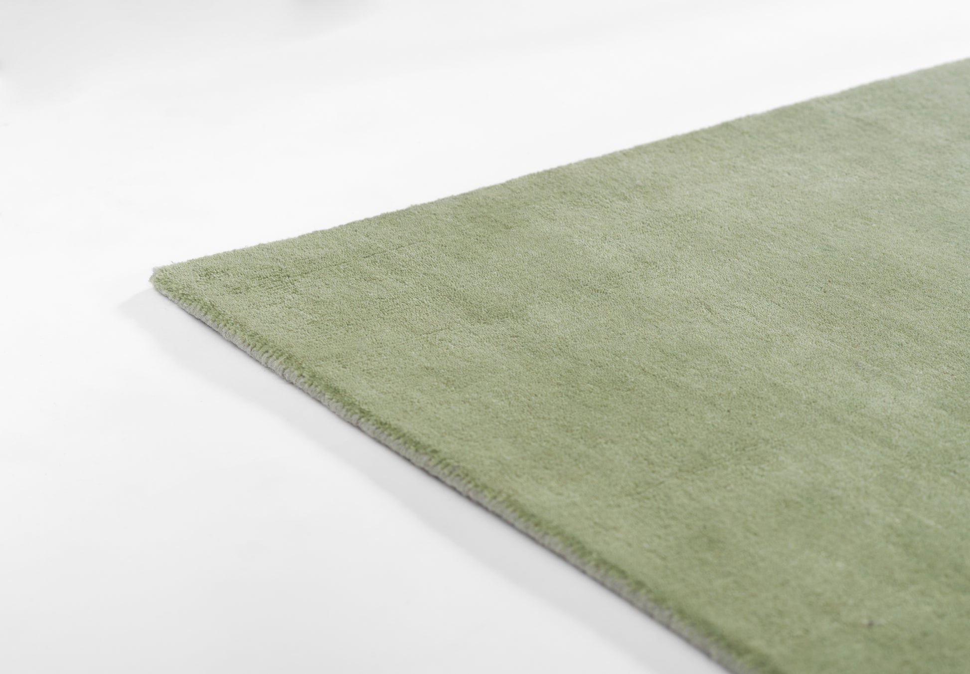 Sage green rectangular rug with soft plush pile; close-up corner view.