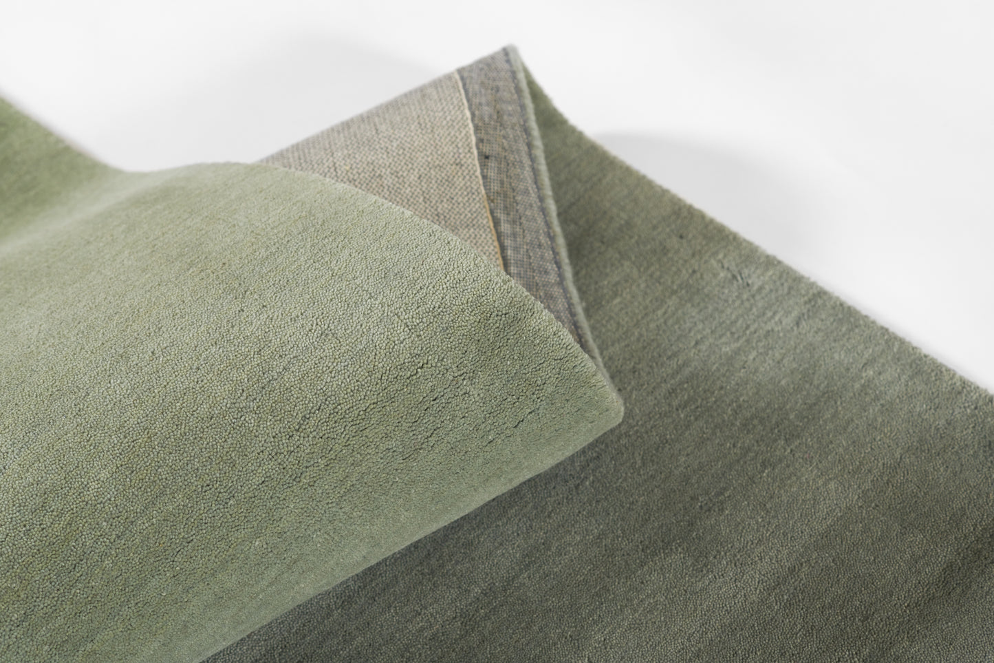 Green ombre rug with soft suede-like pile, light sage to olive gradient, rolled corner.