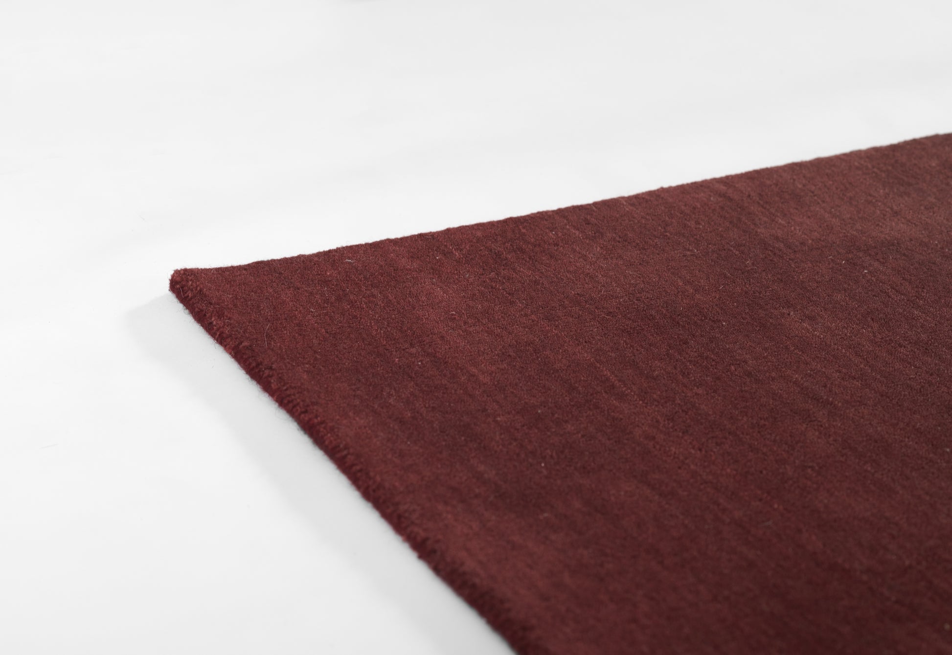Burgundy rectangular rug with soft plush texture and a visible corner against a white backdrop.