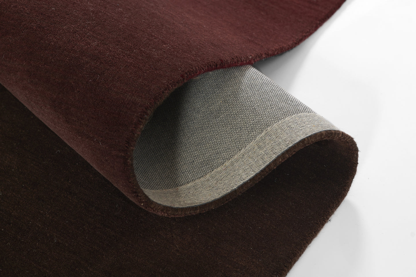 Dark burgundy suede-like fabric rolled to reveal gray woven backing, thick soft throw rug material.