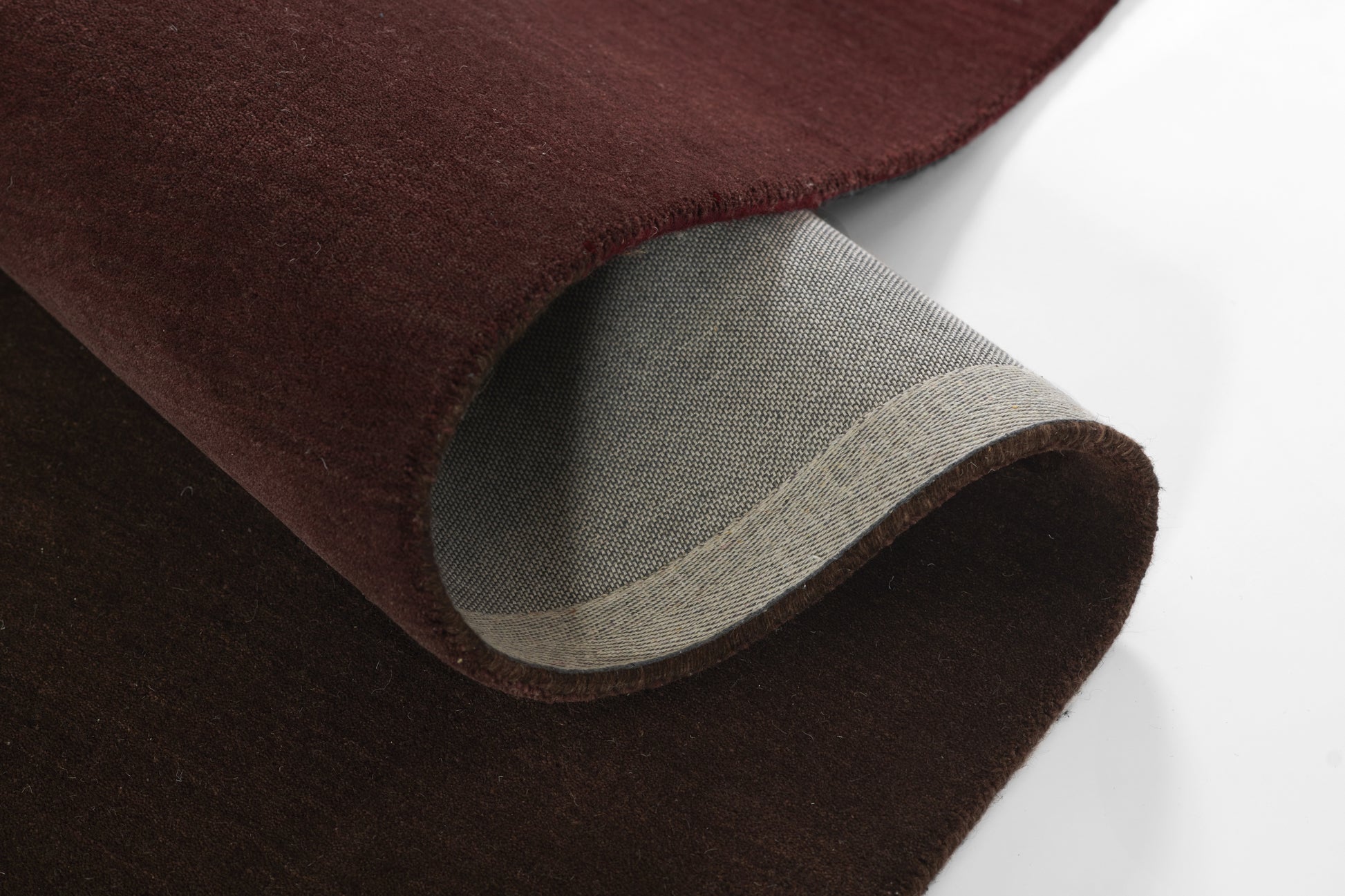 Dark burgundy velvet fabric with light gray woven backing; curved rolled edge swatch, a soft suede-like textile.