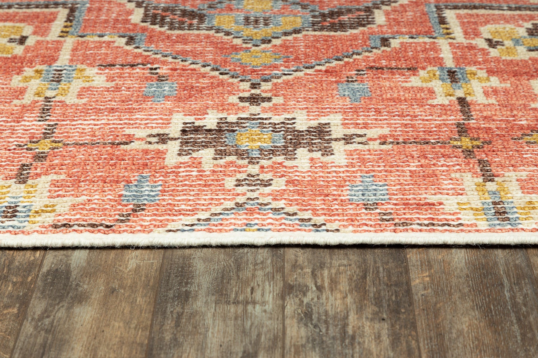 Red geometric patterned rug with ivory fringe and blue/yellow accents on dark wood floor.