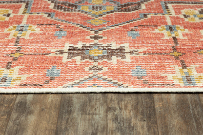 Red oriental-style woven rug with blue and yellow accents and white fringe on a dark wood floor.