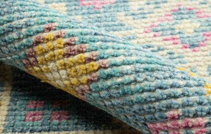 Close-up of a thick, turquoise woven rug with pink, yellow and white accents; soft looped pile texture.