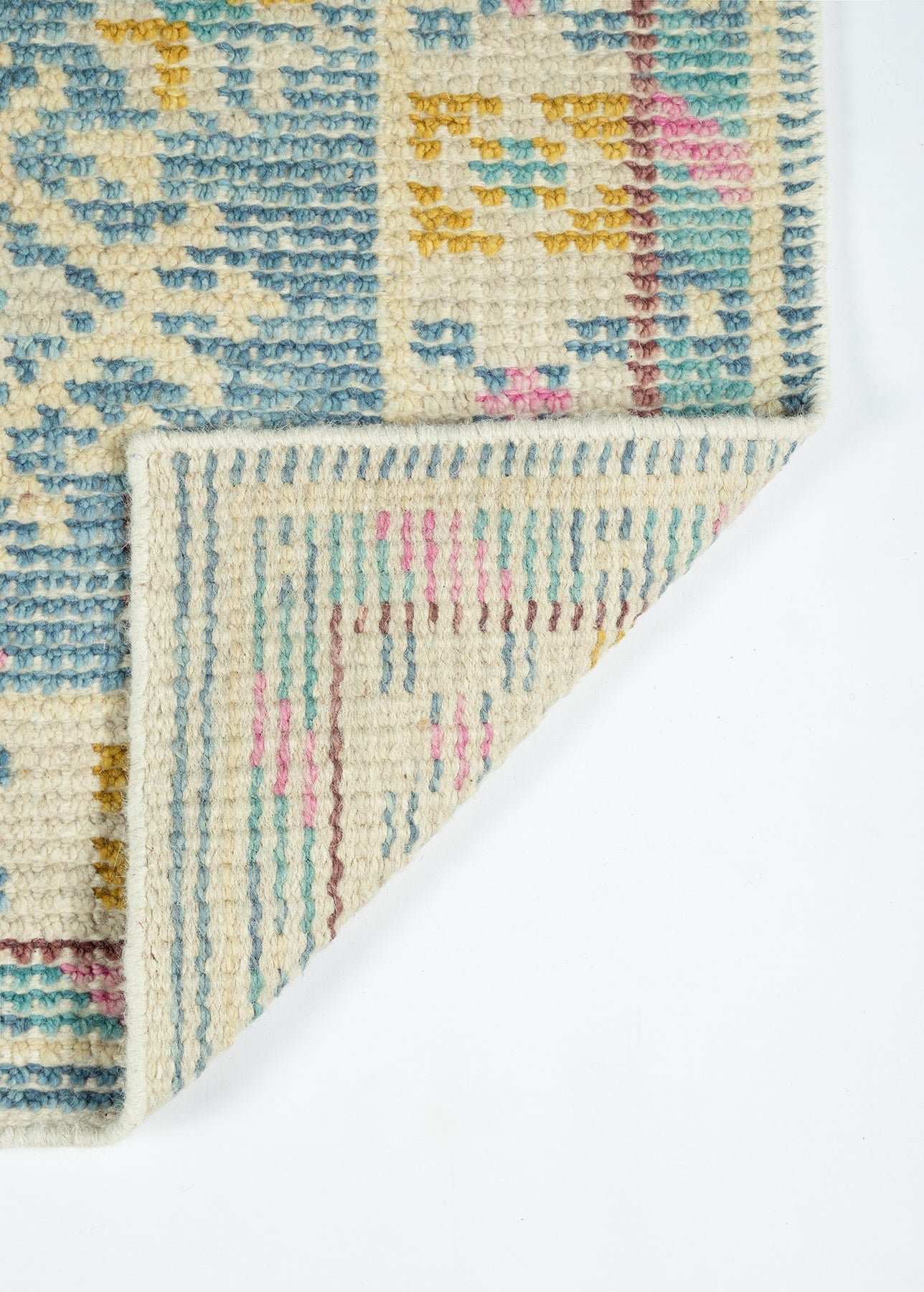 Pastel woven wool rug with blue, cream, pink and yellow geometric patterns; folded corner reveals underside.